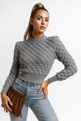 Women's gray textured knit sweater with puff sleeves and ribbed hem, styled with light blue jeans and brown fringe clutch