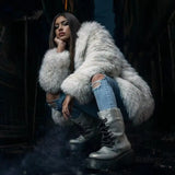 Woman wearing a white faux fur coat with ripped jeans and winter boots posing in a dark urban alley at night